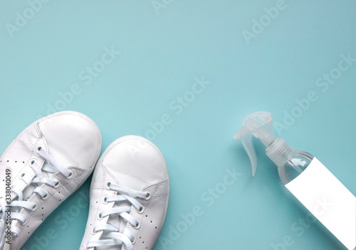 White sneakers and hygienic product for protection and prevention from bacteria and viruses . Antiseptic disinfectant spray bottle with an empty label for your text on light blue background.