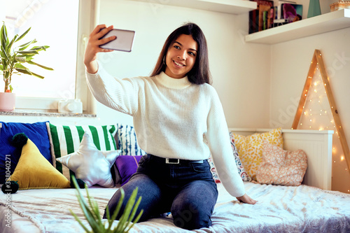 Urban fashion young girl holding cellphone and sitting on bed.