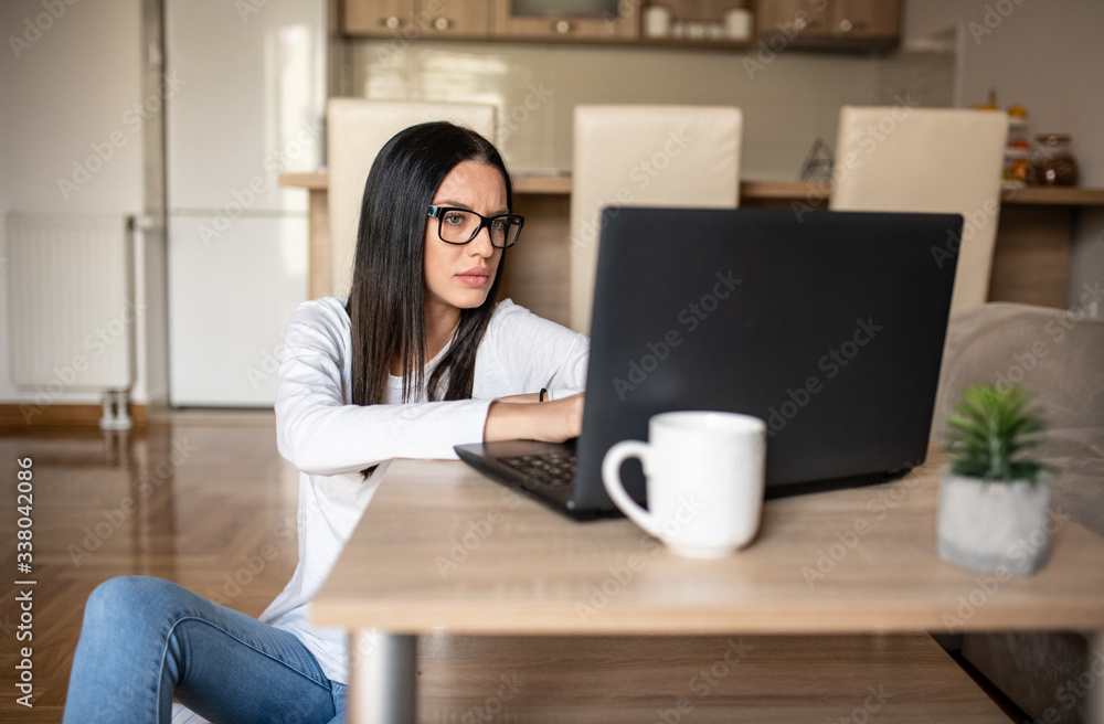 Woman sitting on her kitchens floor looking at her laptop, working.
