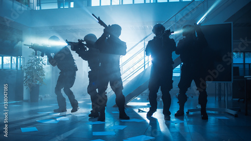 Masked Fireteam of Armed SWAT Police Officers Storm a Dark Seized Office Building with Desks and Computers. Soldiers with Rifles and Flashlights Move Forwards and Cover Surroundings. © Gorodenkoff