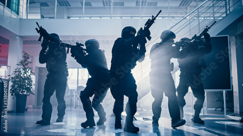Masked Fireteam of Armed SWAT Police Officers Storm a Bright Seized Office Building with Desks and Computers. Soldiers with Rifles Move Forwards and Cover Surroundings. photo
