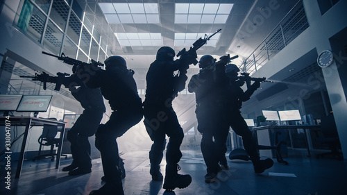 Masked Team of Armed SWAT Police Officers Move in a Hall of a Dark Seized Office Building with Desks and Computers. Soldiers with Rifles and Flashlights Surveil and Cover Surroundings. © Gorodenkoff