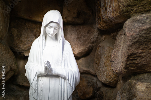 a praying statue of the Virgin Mary in a stone background.
