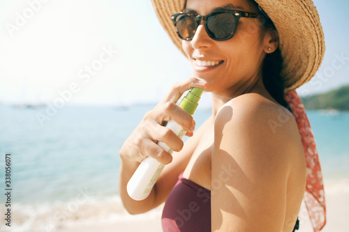 Attractive Young Woman Applying Sunscreen on Tropical Island Beach. Happy Girl in Bikini and Sunglasses Spraying Sun Protection Lotion on Skin. Phuket, Thailand.