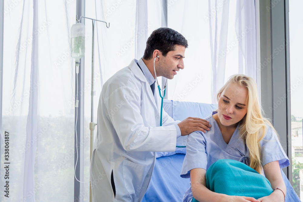 Caucasian female patient in bed and doctor use stethoscope analyze symptom sick at hospital Caucasian female patient in bed and doctor use stethoscope analyze symptom sick at hospital
