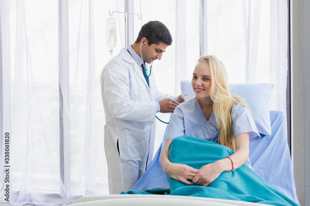 Caucasian female patient in bed and doctor use stethoscope analyze symptom sick at hospital Caucasian female patient in bed and doctor use stethoscope analyze symptom sick at hospital