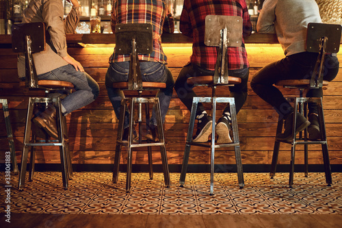 Foto Rear view friends sitting on chairs talking at the bar in a bar.