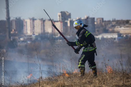 Grass burns in the field Firefighter works against the background of the city.