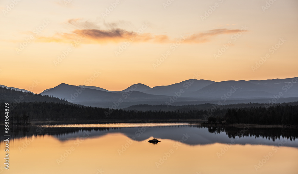 colorful sunset in sweden over a mountain range with still lake in foreground and clean reflections during golden hour in late summer