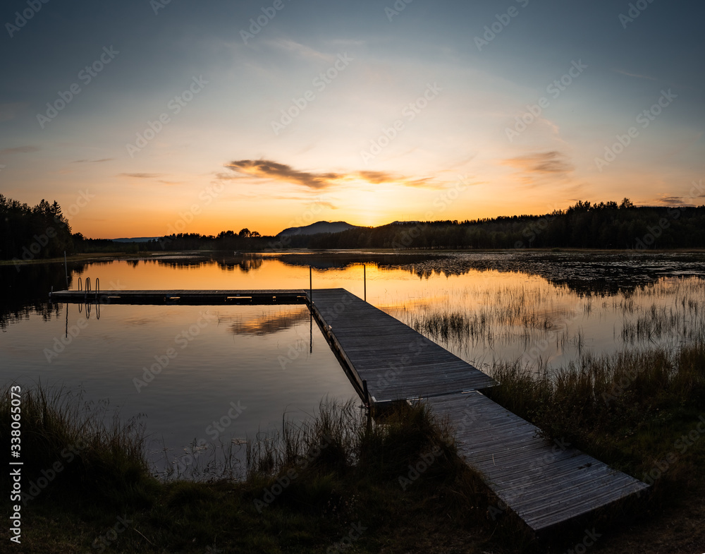 Naklejka premium warm sunset over a pier in sweden with clouds and reflections in the lake