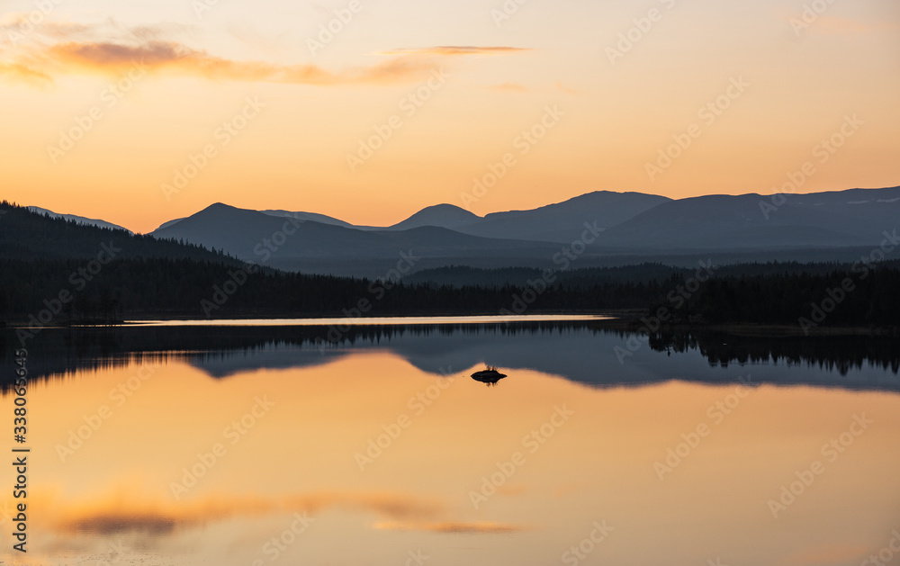 colorful sunset in sweden over a mountain range with still lake in foreground and clean reflections during golden hour in late summer
