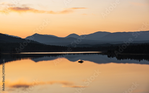 colorful sunset in sweden over a mountain range with still lake in foreground and clean reflections during golden hour in late summer © stalmphotos