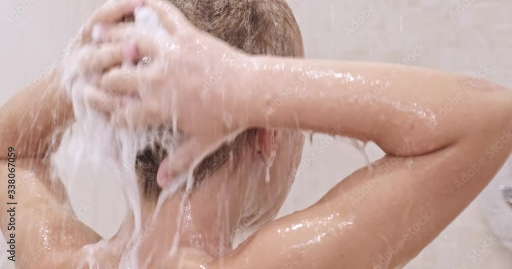 Rear view of a little boy soaps hair with shampoo in the shower. Child takes shower in the bathroom. Kid washes under stream of warm water. European boy rinses hair with water. Slow motion. Rear view of a little boy soaps hair with shampoo in the shower. Child takes shower in the bathroom. Kid washes under stream of warm water. European boy rinses hair with water. Slow motion.
