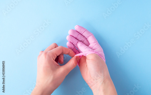 Two female hands in pink rubber medical gloves remove glove on blue background. The concept of treatment, protection from viruses, flu, recovery, stop coronavirus. Flat lay, top view, copy space