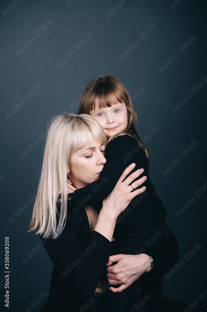 Pretty and charming mother and daughter with beaming smiles over dark blue background.