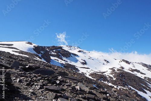 The mountain landscape with the dark rocks covered by white snow, the far top of Mulhacen mountain, the clean blue sky. photo