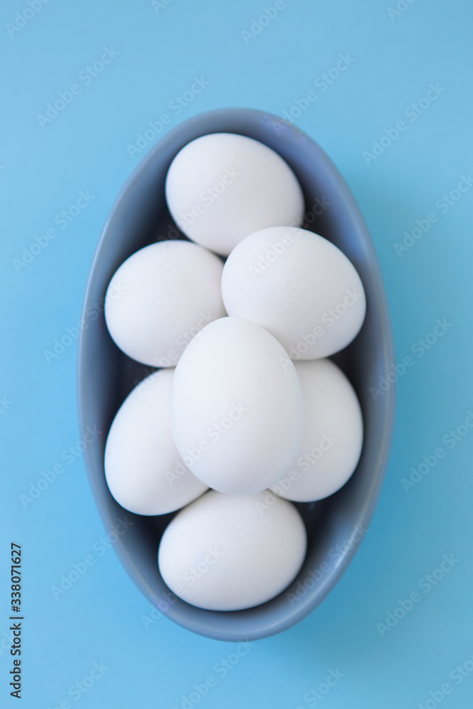 White eggs in bowl on blue background