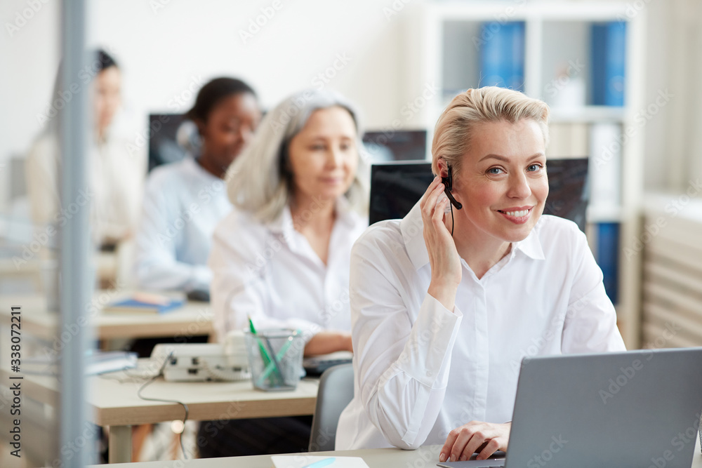 Fototapeta premium Portrait of smiling young woman wearing headset and looking at camera while working as call center operator, copy space