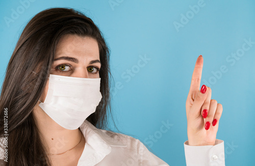 Beautiful girl in white medical mask shows thumb up, blue background