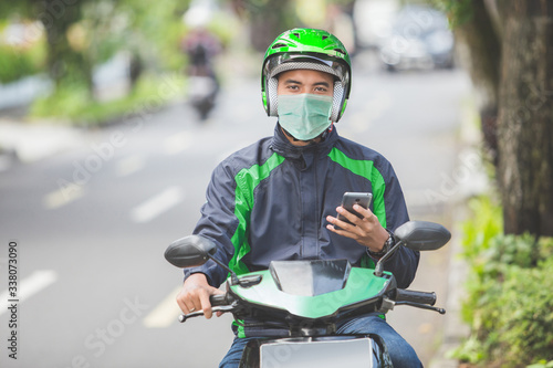 portrait of happy asian man work as a commercial motorcyle taxi driver taking order from his smartphone photo