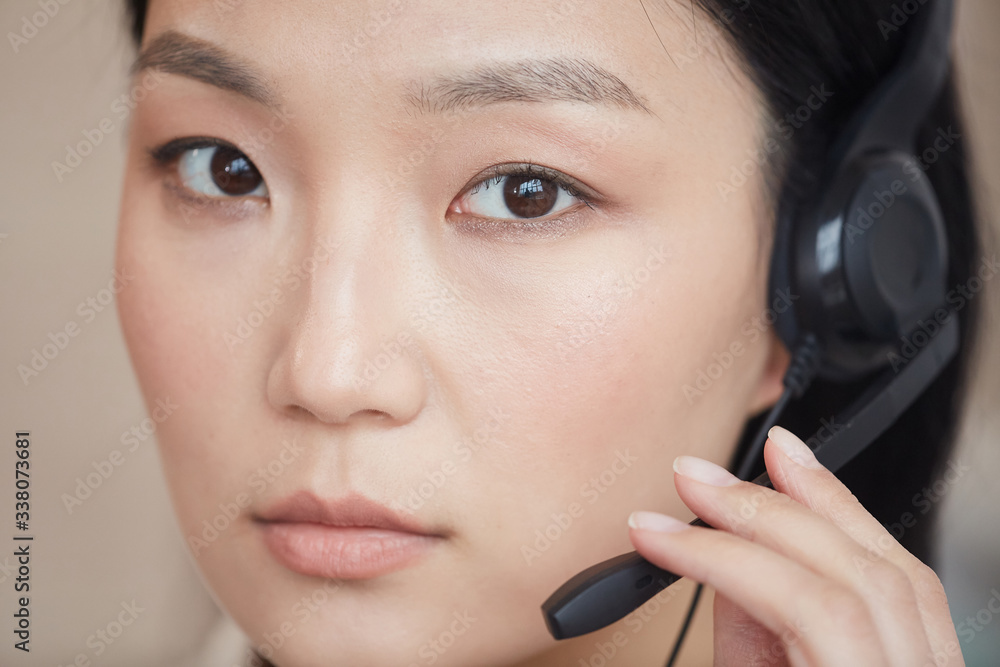 Close up young Asian woman wearing headset and looking at camera while working in support service call center, copy space Close up young Asian woman wearing headset and looking at camera while working in support service call center, copy space