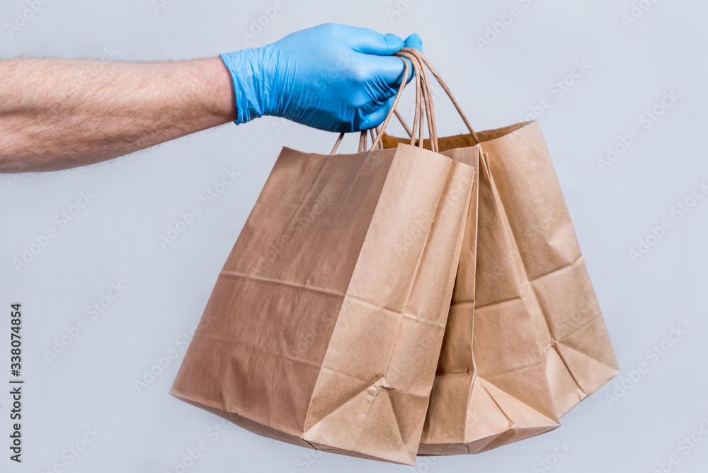 The concept of safe delivery in close-up. the courier's hand in protective medical gloves holds a paper bag. contactless delivery of orders in quarantine during the coronavirus pandemic. The concept of safe delivery in close-up. the courier's hand in protective medical gloves holds a paper bag. contactless delivery of orders in quarantine during the coronavirus pandemic.
