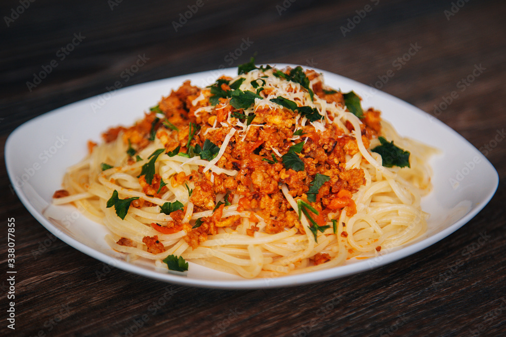 Spaghetti with minced meat in tomato with herbs and cheese on a white plate. Plate with food on a dark wooden table. Lunch with meat. Spaghetti with minced meat in tomato with herbs and cheese on a white plate. Plate with food on a dark wooden table. Lunch with meat.