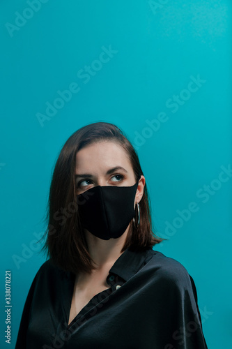 A fashionable girl in a black medical mask and black evening dress looks up to the right