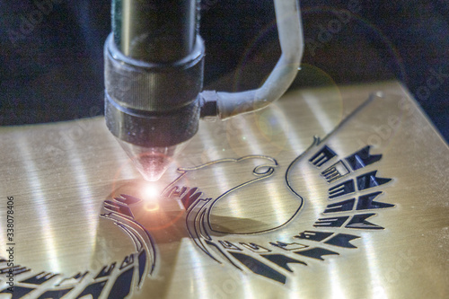 A laser engraving machine cuts out a picture on a gold glossy plastic plate. Closeup