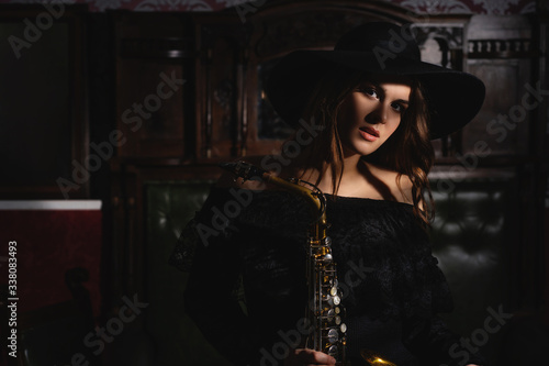girl in a retro hat and dress with a saxophone in hands.