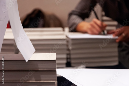 Books stacked and hands signing book in the background out of focus photo