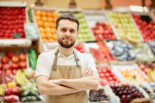 Fotografie Waist up portrait of bearded man looking at camera while standing by fruit and v