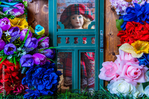 young girl doll looking out of miniature screen door at colorful spring flowers photo