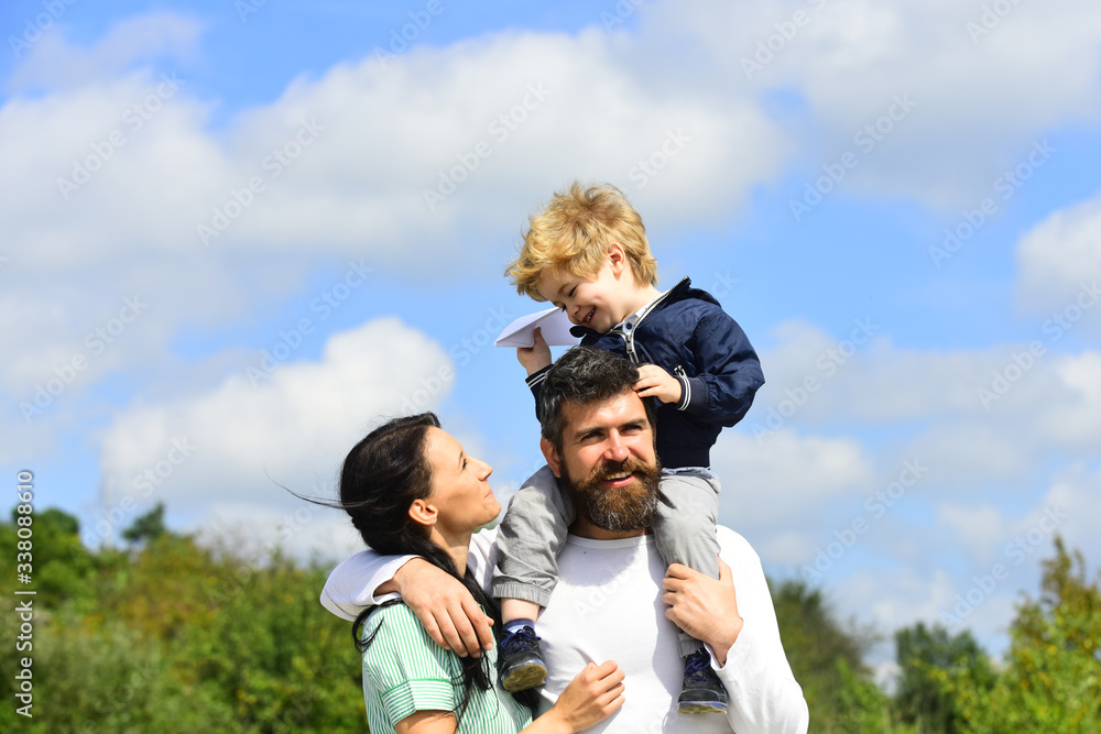 Happy family - mother, father and son on sky background in summer. Happy child playing with toy paper plane against summer sky background. Father and son enjoying outdoor. Happy family - mother, father and son on sky background in summer. Happy child playing with toy paper plane against summer sky background. Father and son enjoying outdoor.