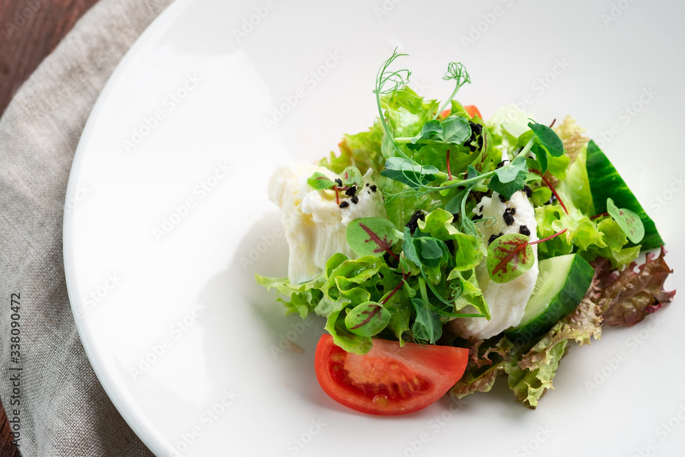 Light diet salad of mozzarella and fresh vegetables -cucumber, tomato, lettuce, peas on a white plate on a wooden background Light diet salad of mozzarella and fresh vegetables -cucumber, tomato, lettuce, peas on a white plate on a wooden background