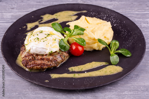 A piece of steak with egg paschot, served with puree potatoes and cherry tomatoes with greens