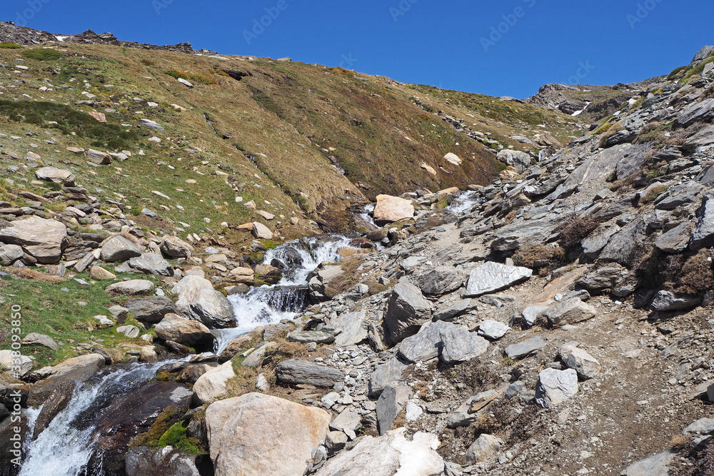 Φωτογραφία The mountain landscape with the small river with waterfalls, the slope covered by green grass, the clean blue sky