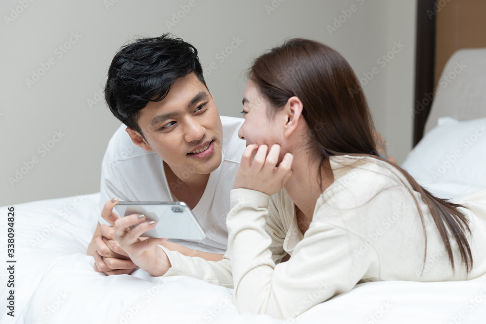 A young Asian couple is playing mobile phone in bed A young Asian couple is playing mobile phone in bed