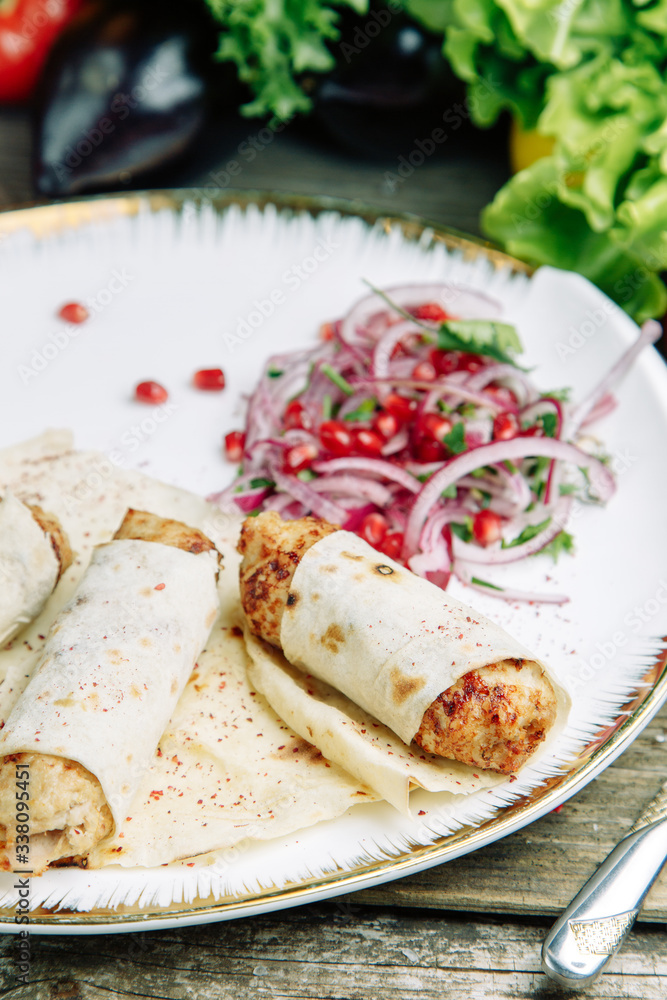 Restaurant dish on a wooden background with vegetables. Lula kebab in lavash with pomegranate and onion on a plate.