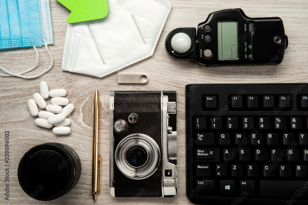 Flat assembly composition with pills, exposure meter, photo lens, keyboard,block notes, masks on white wooden background