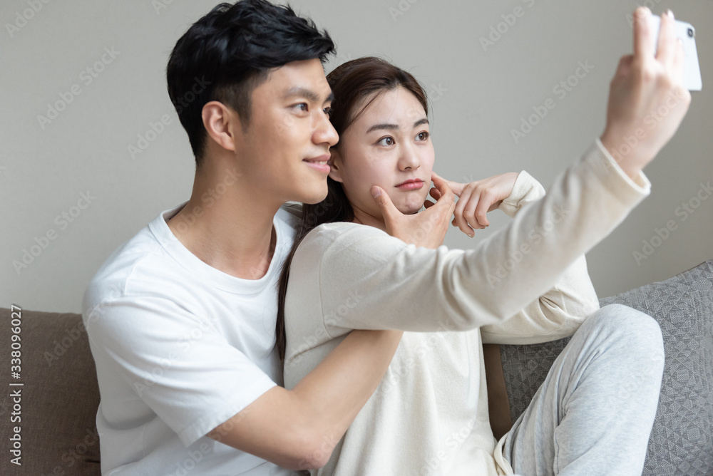 A young Asian couple taking pictures of each other on the sofa A young Asian couple taking pictures of each other on the sofa