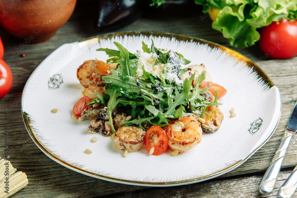  Restaurant dish on a wooden background with vegetables. Salad with shrimp, avocado and arugula on a plate.