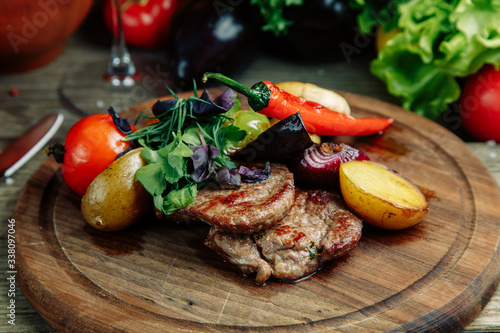 Restaurant dish on a wooden background with vegetables. Steak with vegetables and peppers on a wooden Board.