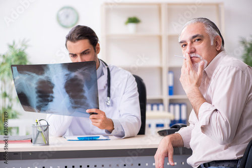 фотографія Young male doctor and old patient in antismoking concept