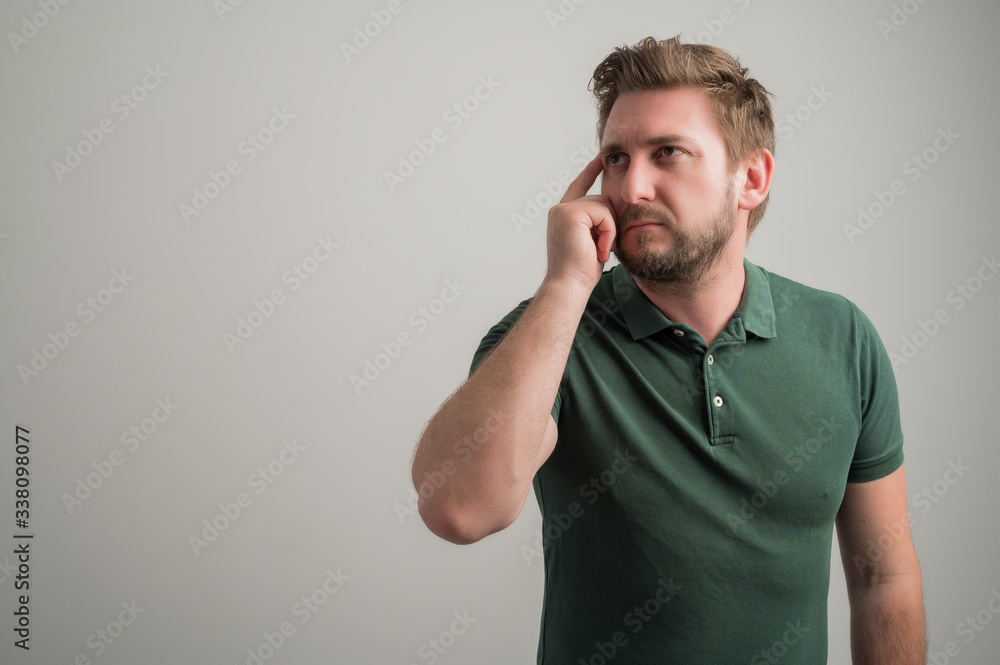 Portrait of serious stylish attractive man with thick beard, dressed in casual green t shirt making thinking gesture Portrait of serious stylish attractive man with thick beard, dressed in casual green t shirt making thinking gesture
