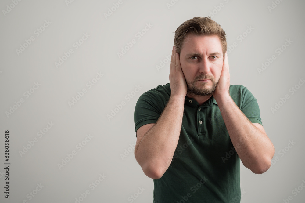 Portrait of serious stylish attractive man with thick beard, dressed in casual green t shirt covering ears like deaf gesture Portrait of serious stylish attractive man with thick beard, dressed in casual green t shirt covering ears like deaf gesture