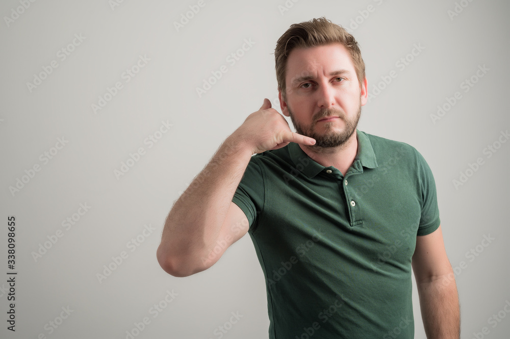 Portrait of serious stylish attractive man with thick beard, dressed in casual green t shirt showing calling or contact gesture Portrait of serious stylish attractive man with thick beard, dressed in casual green t shirt showing calling or contact gesture