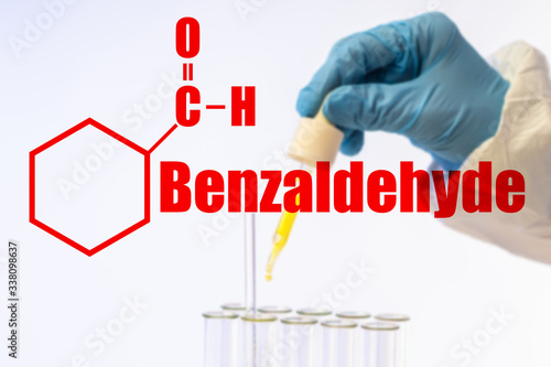 The inscription Benzaldehyde and molecular formula on the background of the chemist's hands. A substance for the synthesis of dyes and scented substances. The simplest aldehyde of the aromatic series.