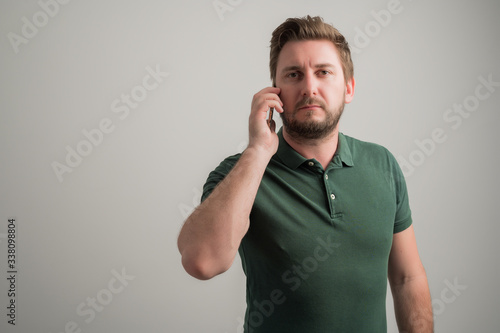Portrait of serious stylish attractive man with thick beard, dressed in casual green t shirt talking on the phone