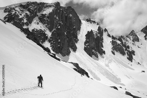 Mountains with avalanche traces, sunlit cloudy sky, hiker and dog on snowy slope